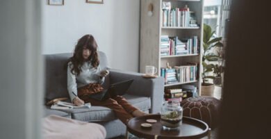 Madre trabajando con su ordenador desde el sofá de su casa